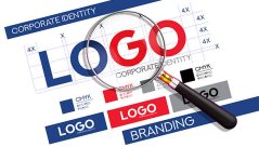 A magnifying glass closely examines a logo on a corporate identity and branding guide, highlighting the meticulous process of brand development. The document includes grid lines for precision, color swatches with CMYK values, and various logo mockups, illustrating the creation of a strong visual identity. This image is perfect for graphic designers, marketing agencies, and businesses to represent concepts like brand strategy, logo creation, quality control, and the importance of a well-defined corporate identity.